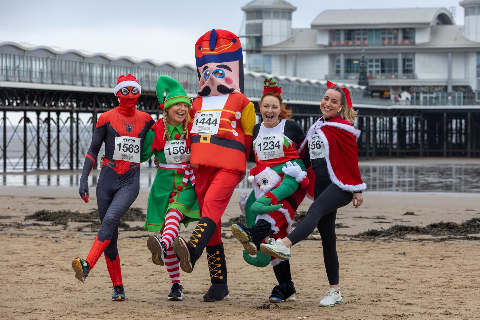 A team of five runners all in festive fancy dress standing in front of Weston's Grand Pier before the annual Weston-super-Mare Christmas Cracker Run